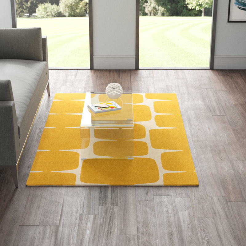 Yellow and white patterned rug on a wooden floor with a gray sofa and glass table in the background.