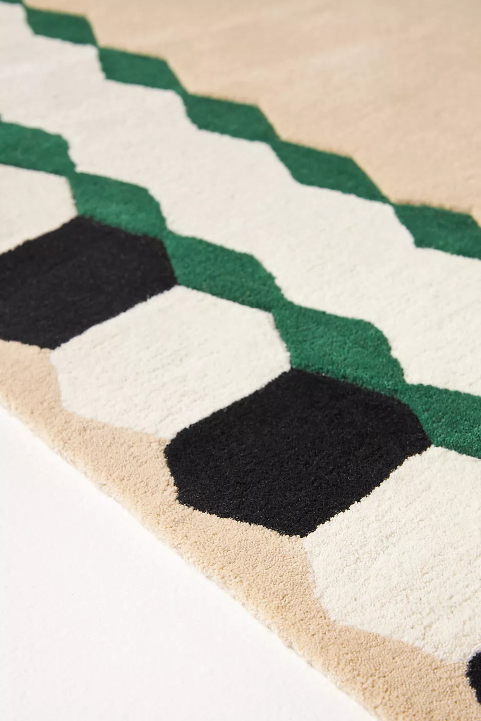 Close-up of a geometric patterned rug with green, black, and beige colors.