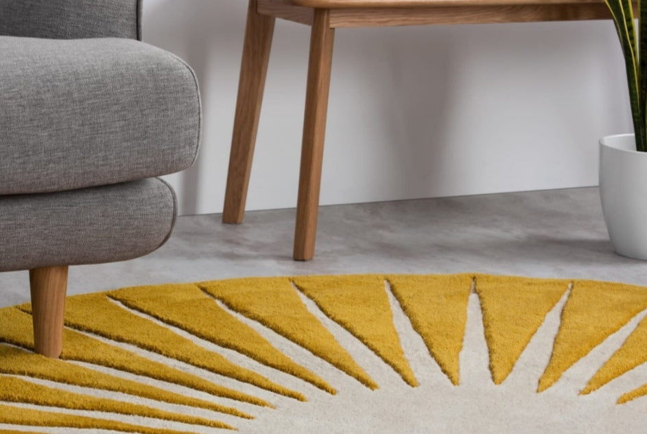 Yellow sunburst handmade rug on a gray floor with a gray chair and wooden table in the background.