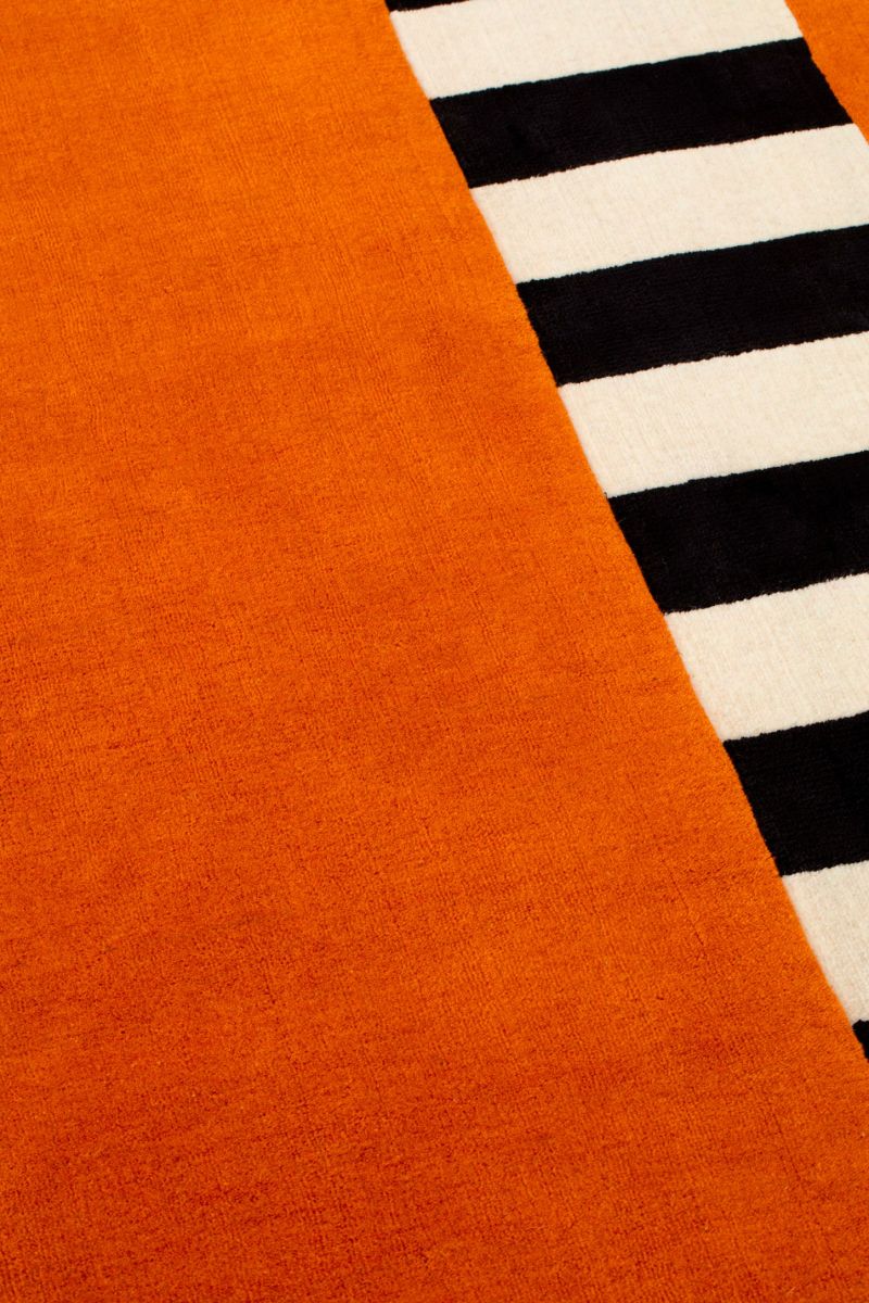 Close-up of an orange rug with a black and white striped pattern.