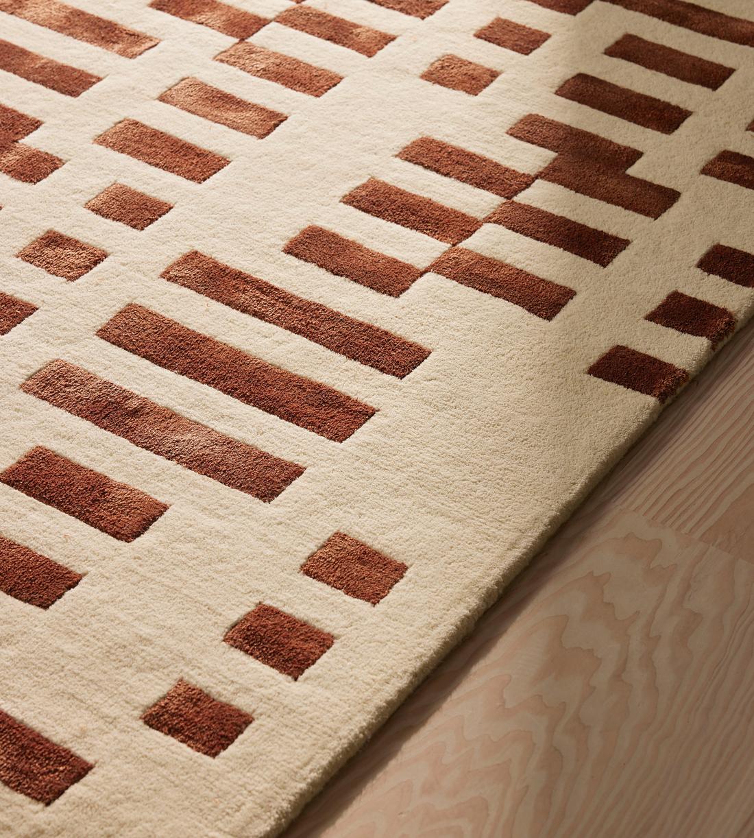 Close-up of a textured rug with brown and beige pattern on a wooden floor.