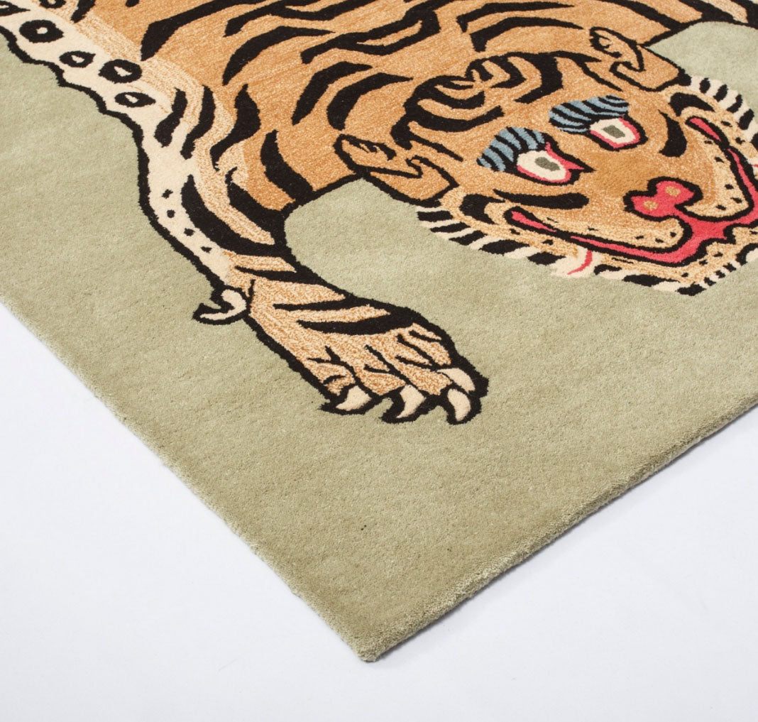 Hand-tufted wool tiger rug featuring a gold and black Tibetan-style tiger motif on a sage green background, full overhead view.