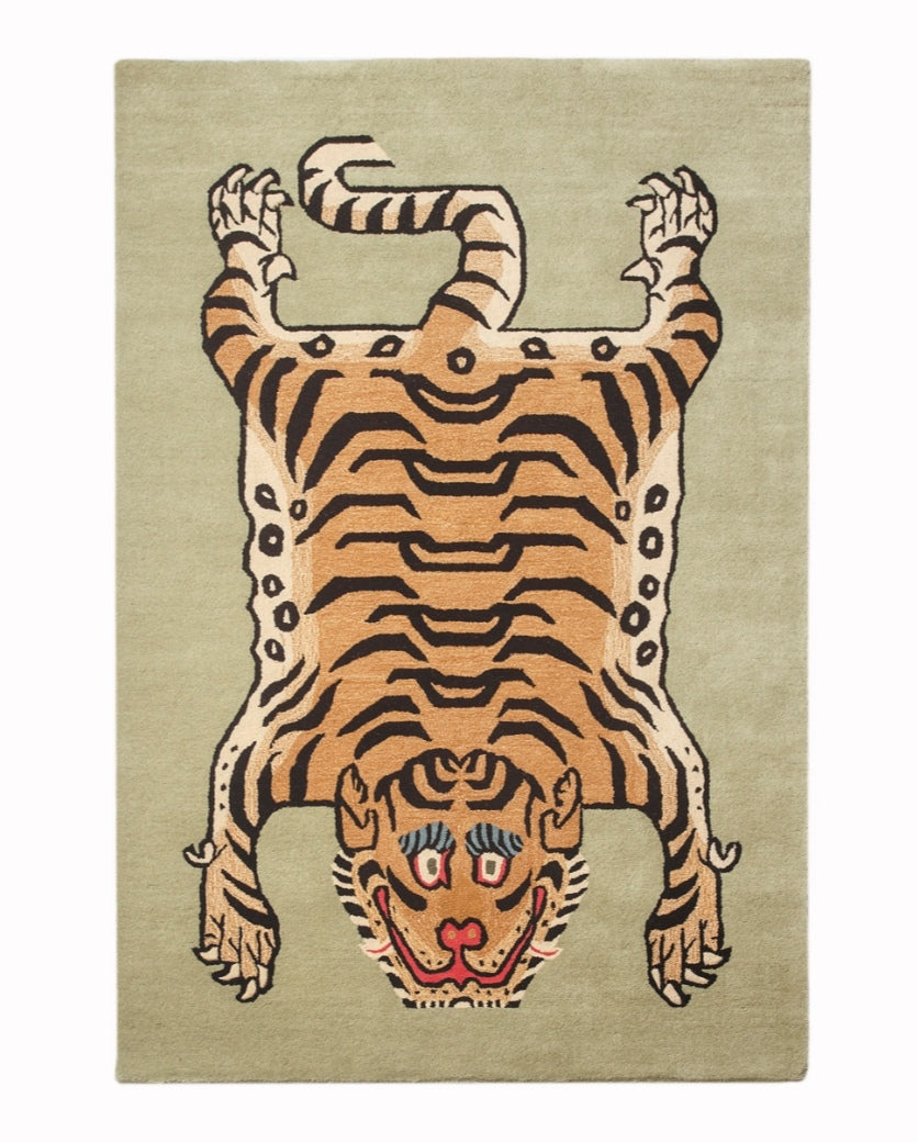 Hand-tufted wool tiger rug with orange and black stripes on a sage green background, overhead view.